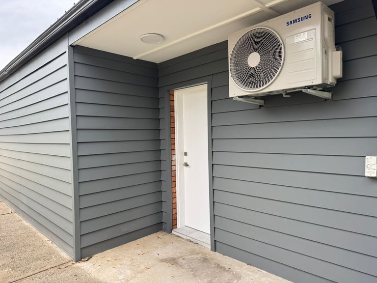 Gray metal shed exterior with white door and Samsung air conditioning unit mounted on wall