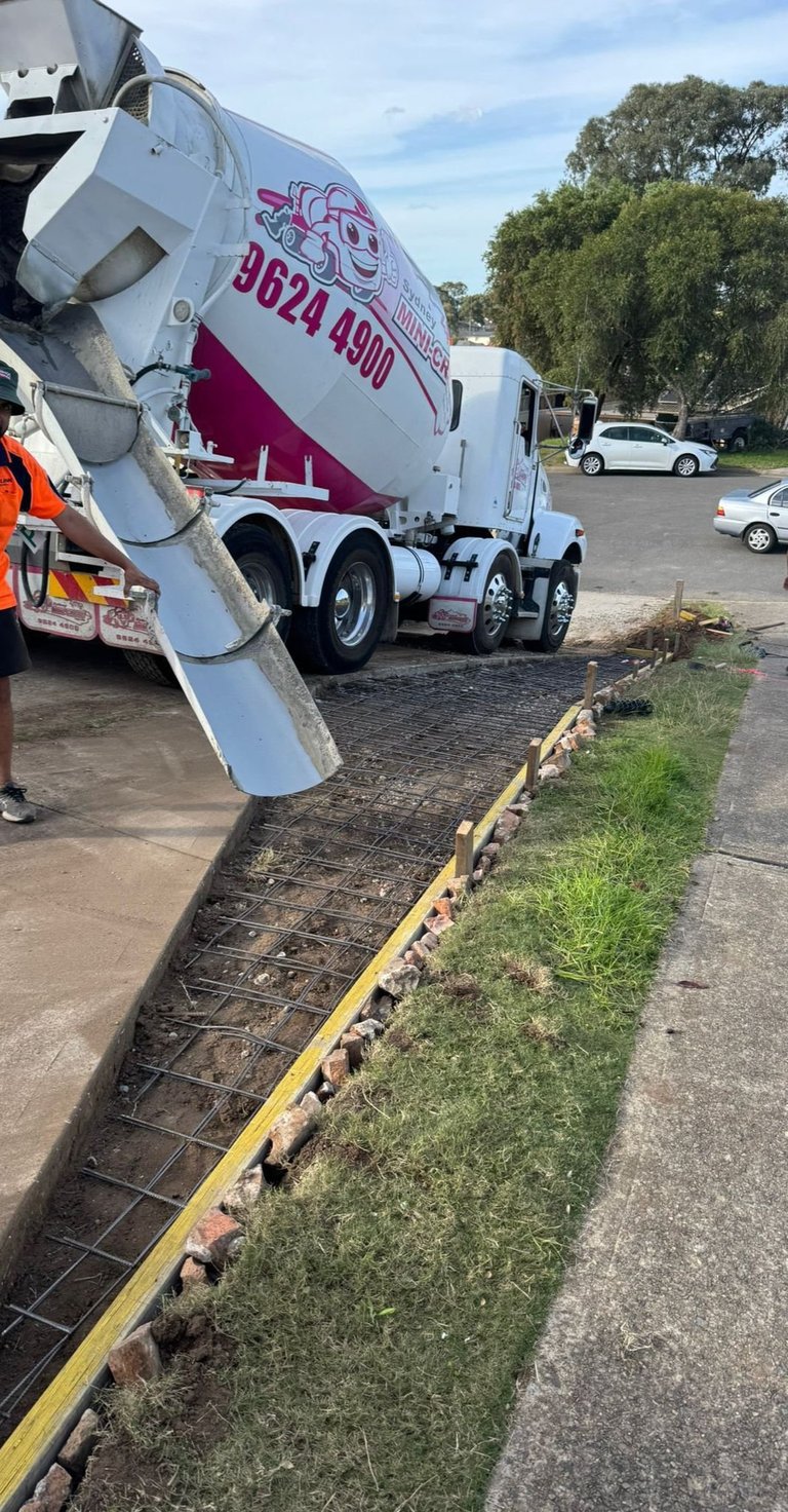 Cement mixer truck with white and pink branding parked in lot near yellow curb and grassy edge