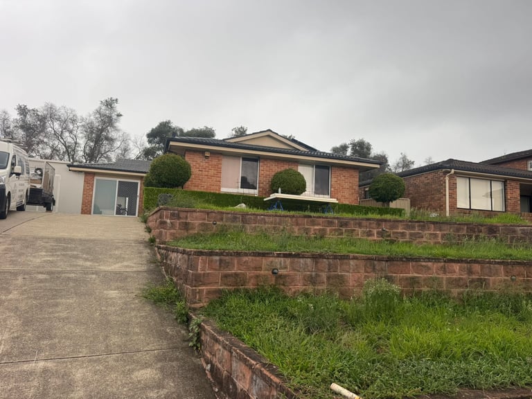 Brick single-story house with driveway and brick retaining wall on overcast day