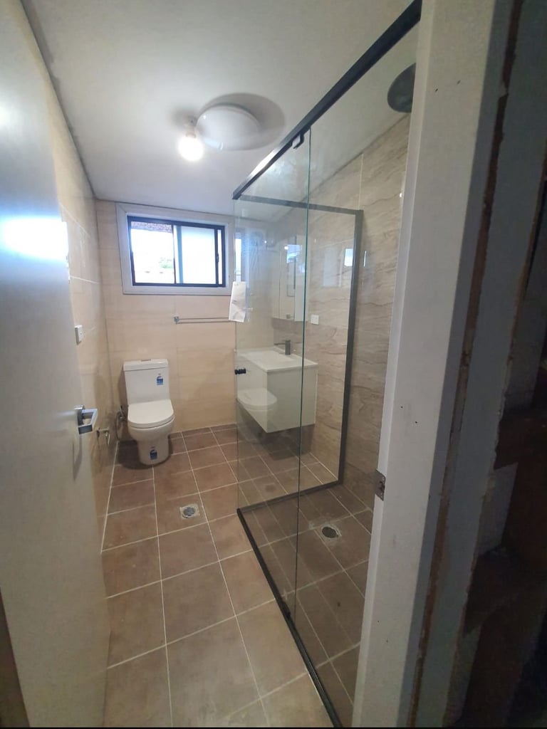 Modern bathroom with large walk-in shower, glass enclosure, toilet, and window with natural lighting