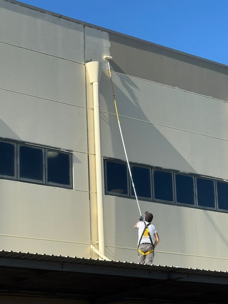 Worker in safety harness rappelling down exterior wall of industrial building with clear sky background