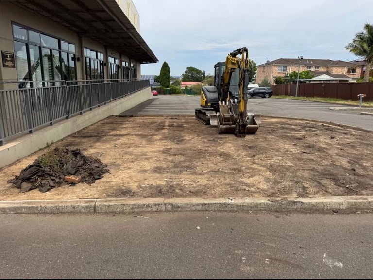Yellow excavator on dirt parking lot next to modern building with striped awning